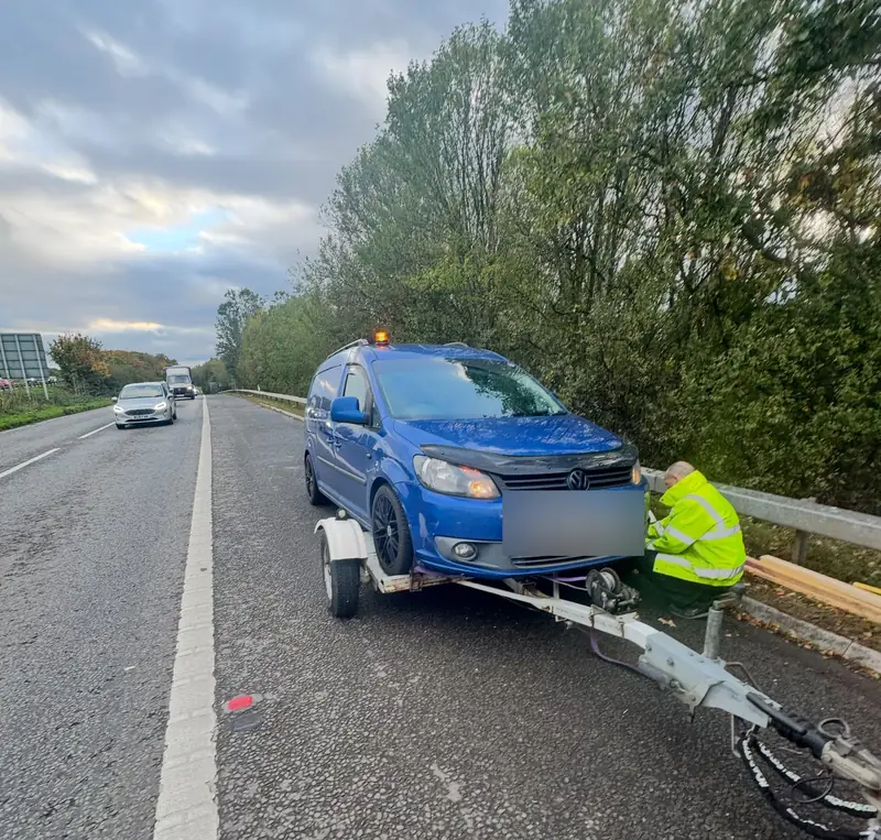 Roadside recovery of a broken-down blue Volkswagen Caddy loaded onto a tow dolly on a dual carriageway